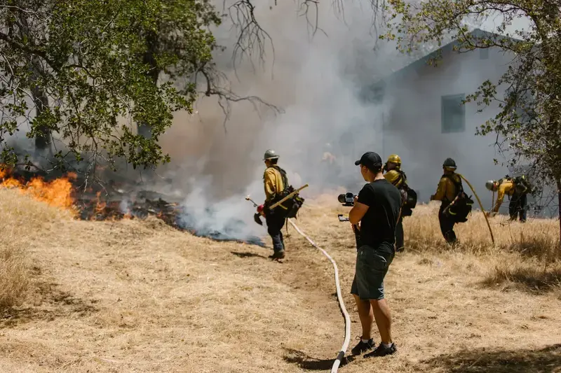 Firefighters fighting wildfire in dry grass near houses