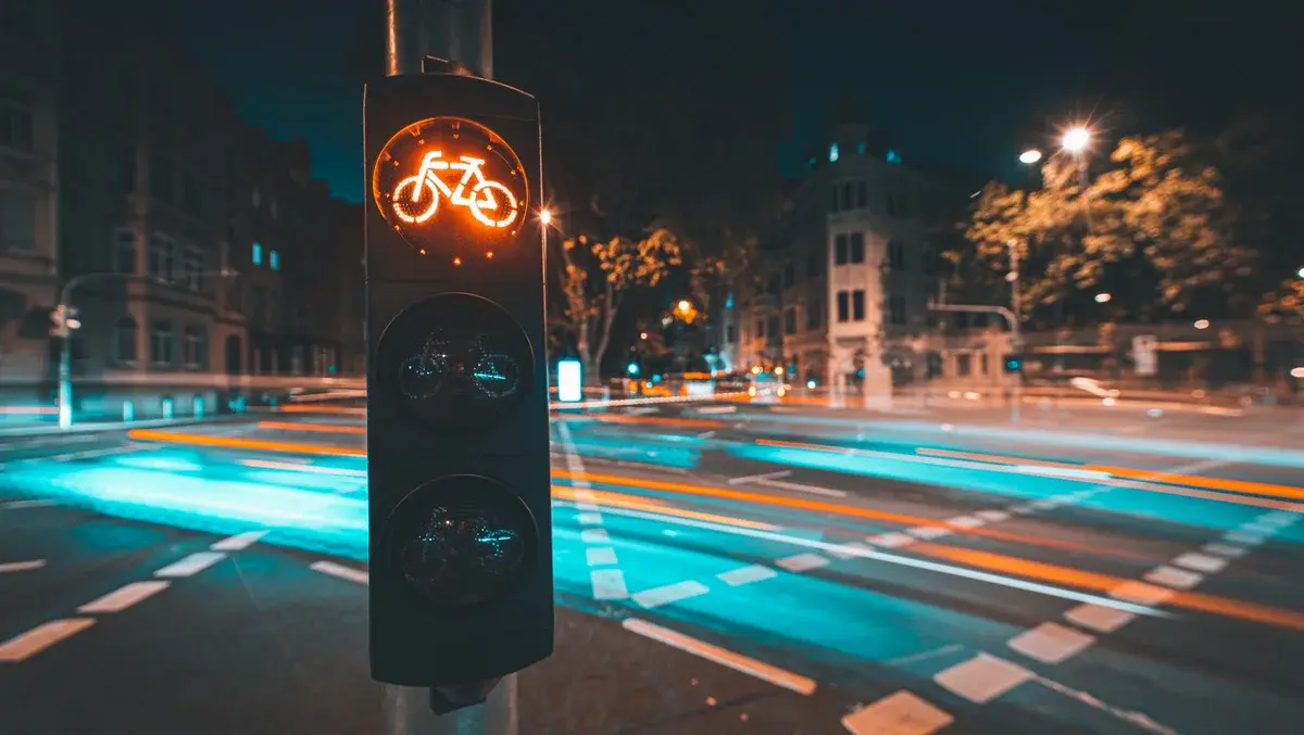 A glowing bicycle traffic light at a night-time city intersection with light trails from passing traffic.