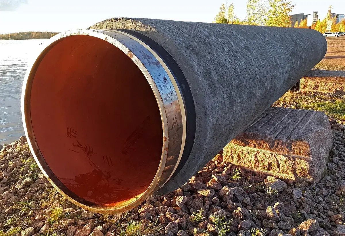 A large pipeline section displayed outdoors beside the water.