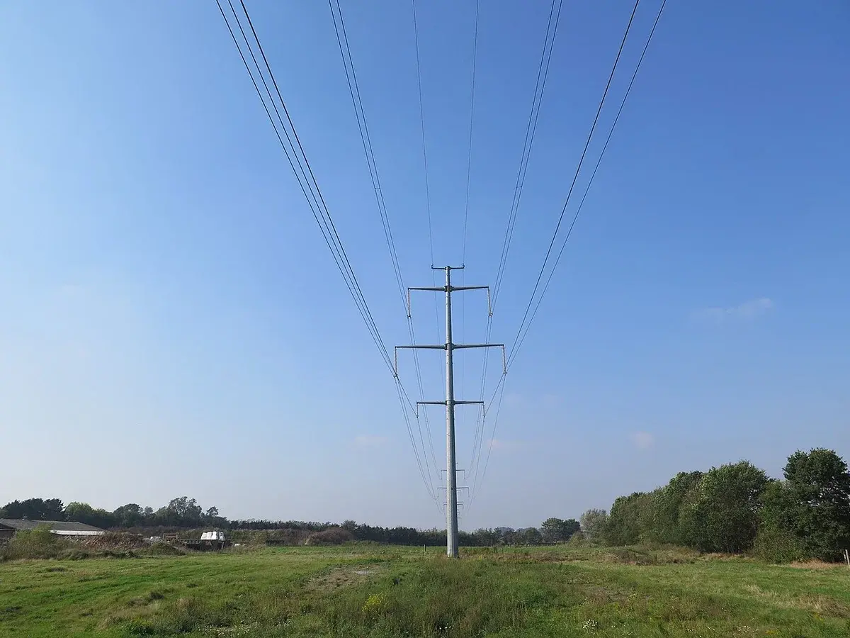 Electricity pylons and power lines over a green field under a clear blue sky