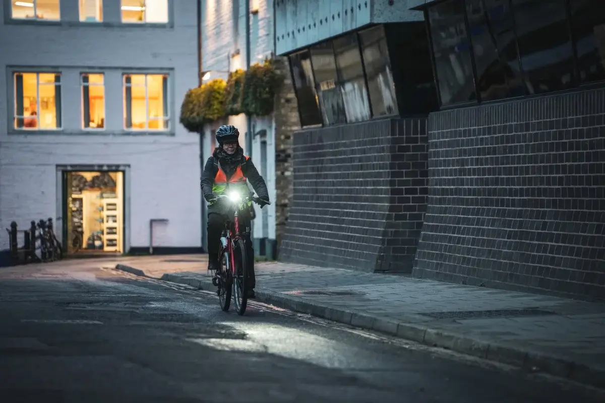 A cyclist riding at night on a city street with a bright front light.