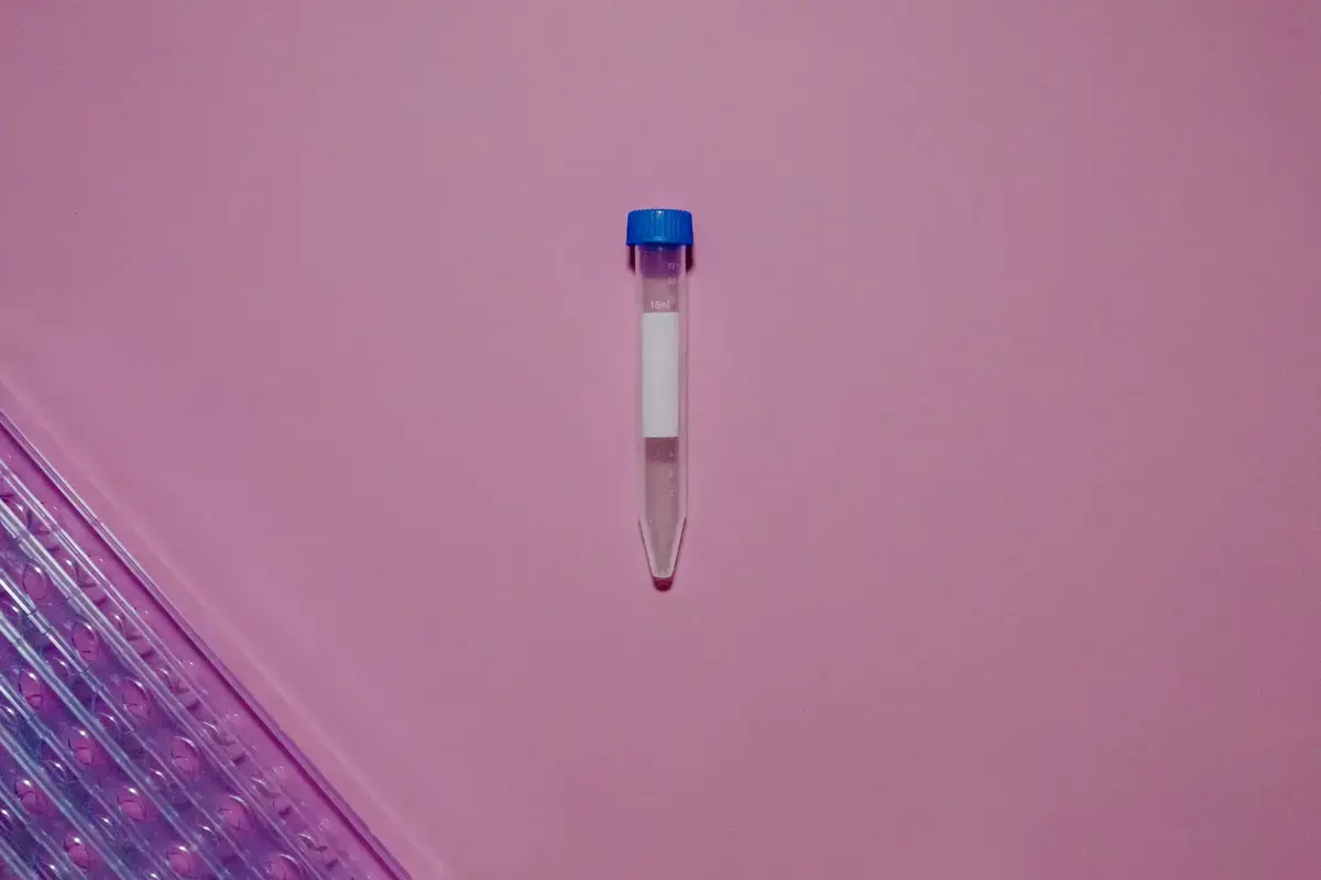 Close-up of a laboratory test tube with blue cap on a vibrant pink background with a glass tray.