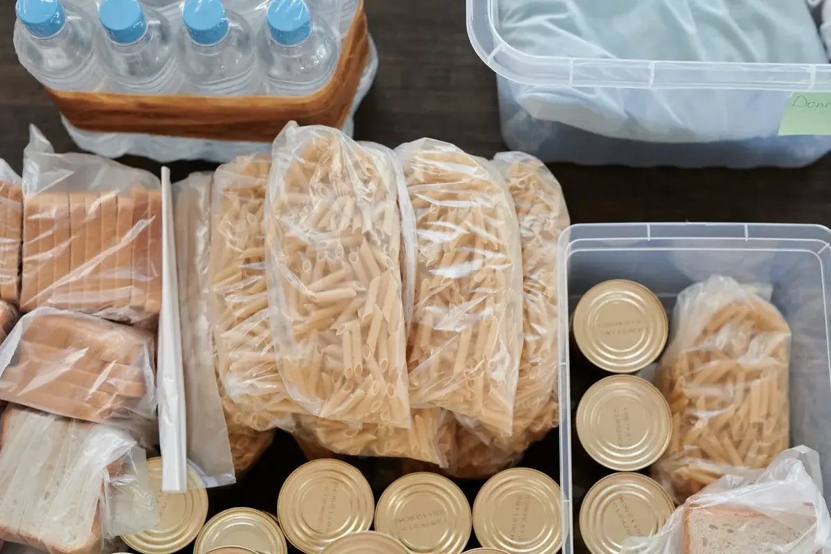 Overhead view of pantry supplies including pasta, canned food, bread, and bottled water packed for storage.