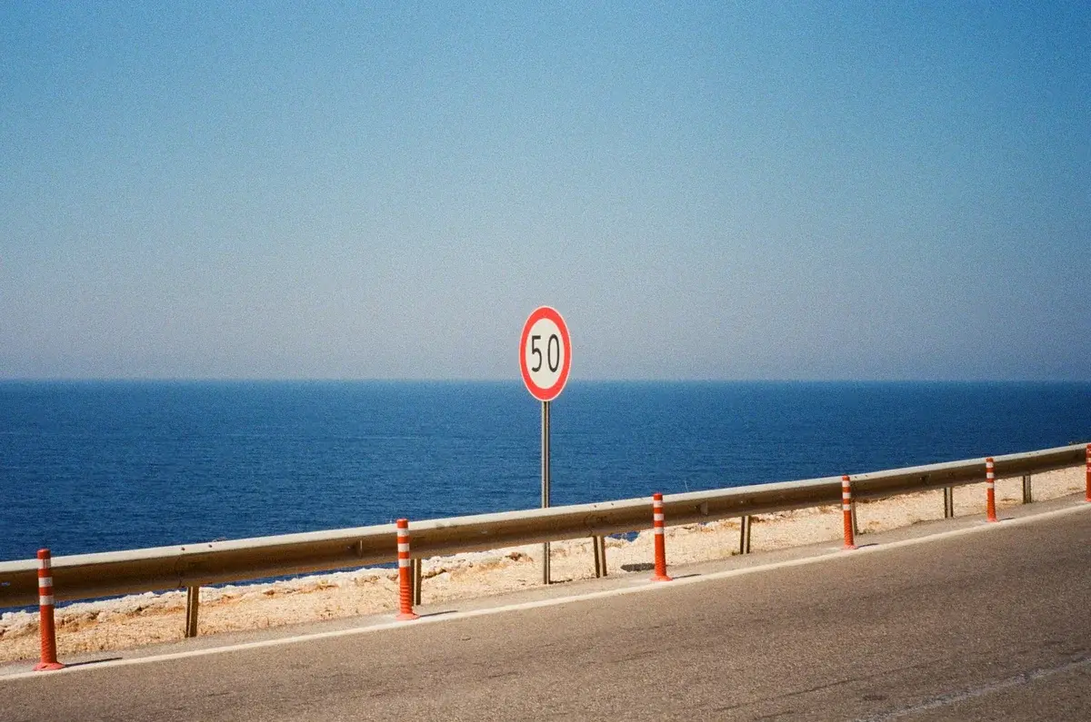 A coastal road with a 50 km/h speed limit sign overlooking the sea.