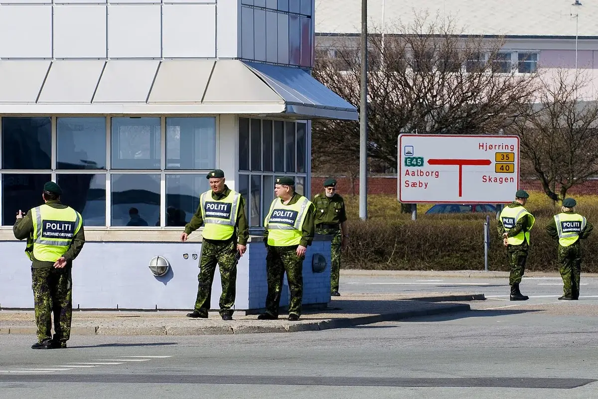 Danish Home Guard officers in high-visibility vests standing on a road corner, managing traffic.