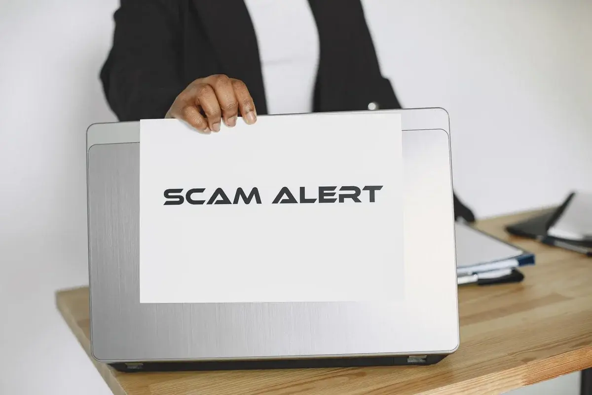 Person holding scam alert sign on laptop
