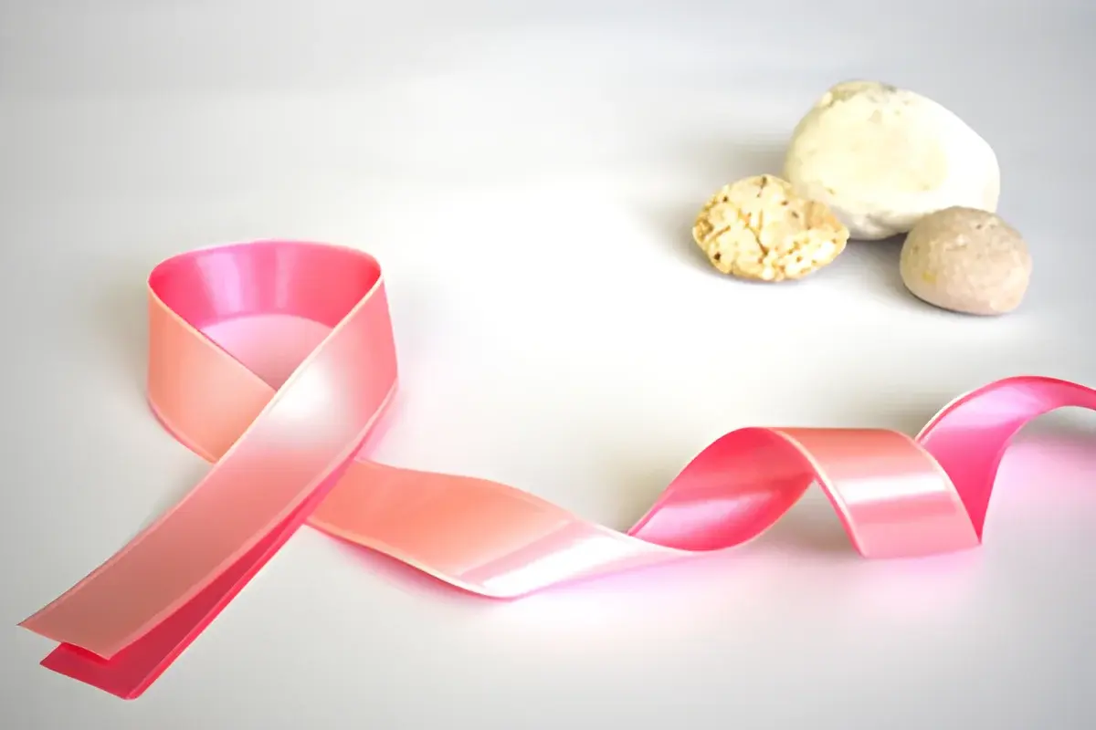 Pink breast cancer awareness ribbon beside three small stones on a white background.