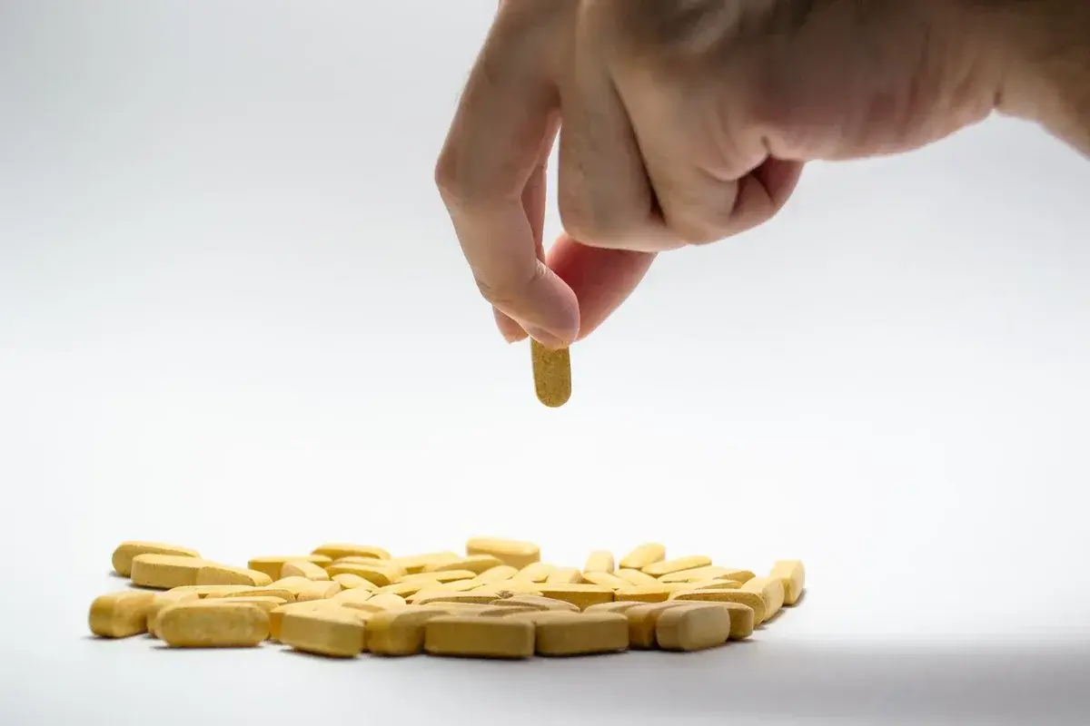 Hand holding a yellow pill above a pile of yellow tablets