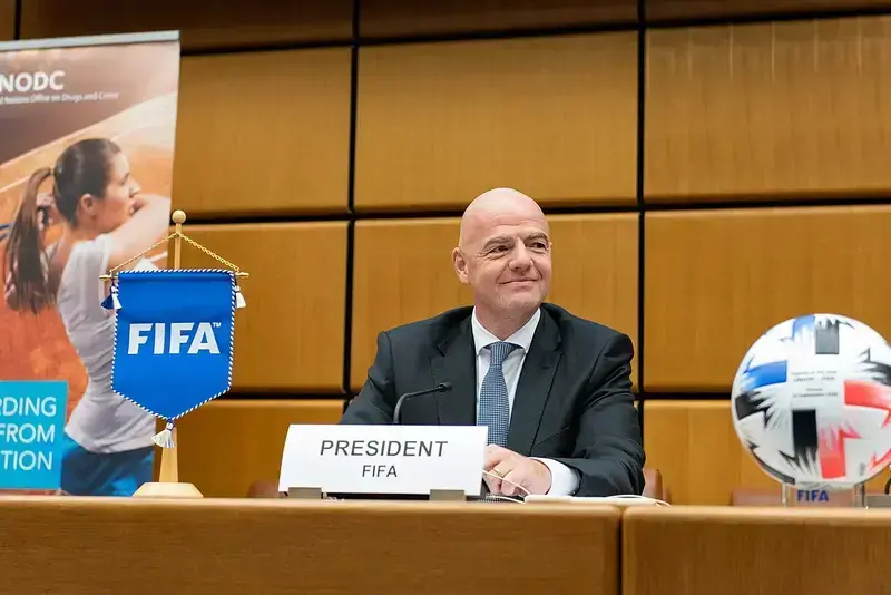 Gianni Infantino sitting at a conference table with a FIFA banner and football