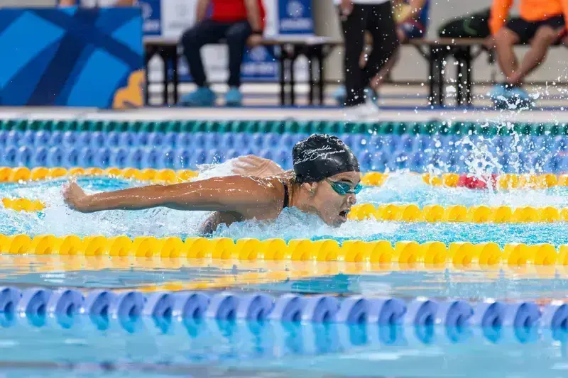 Swimmer performing butterfly stroke in pool during competition