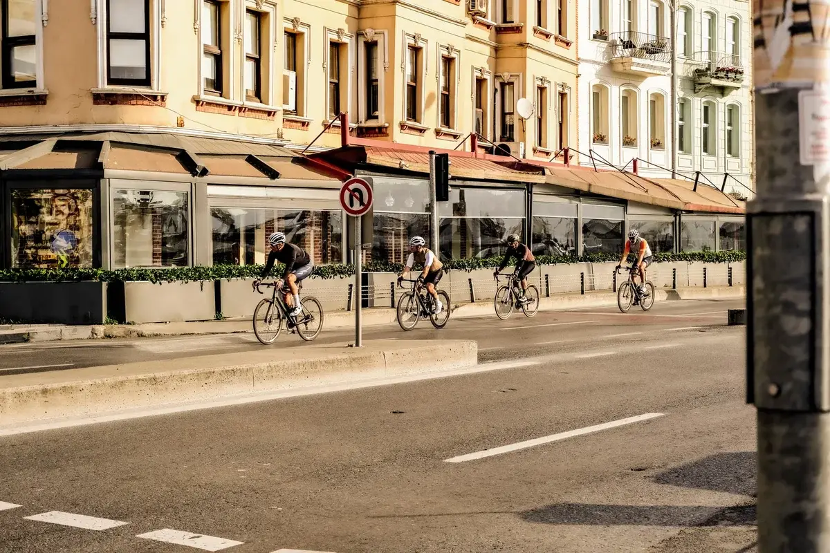 Four cyclists ride along a city street beside historic buildings.