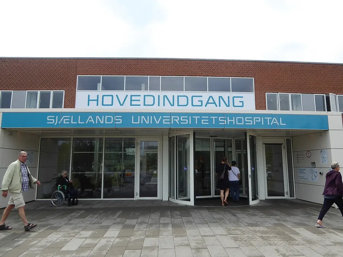 Main entrance of Zealand University Hospital with people walking by.