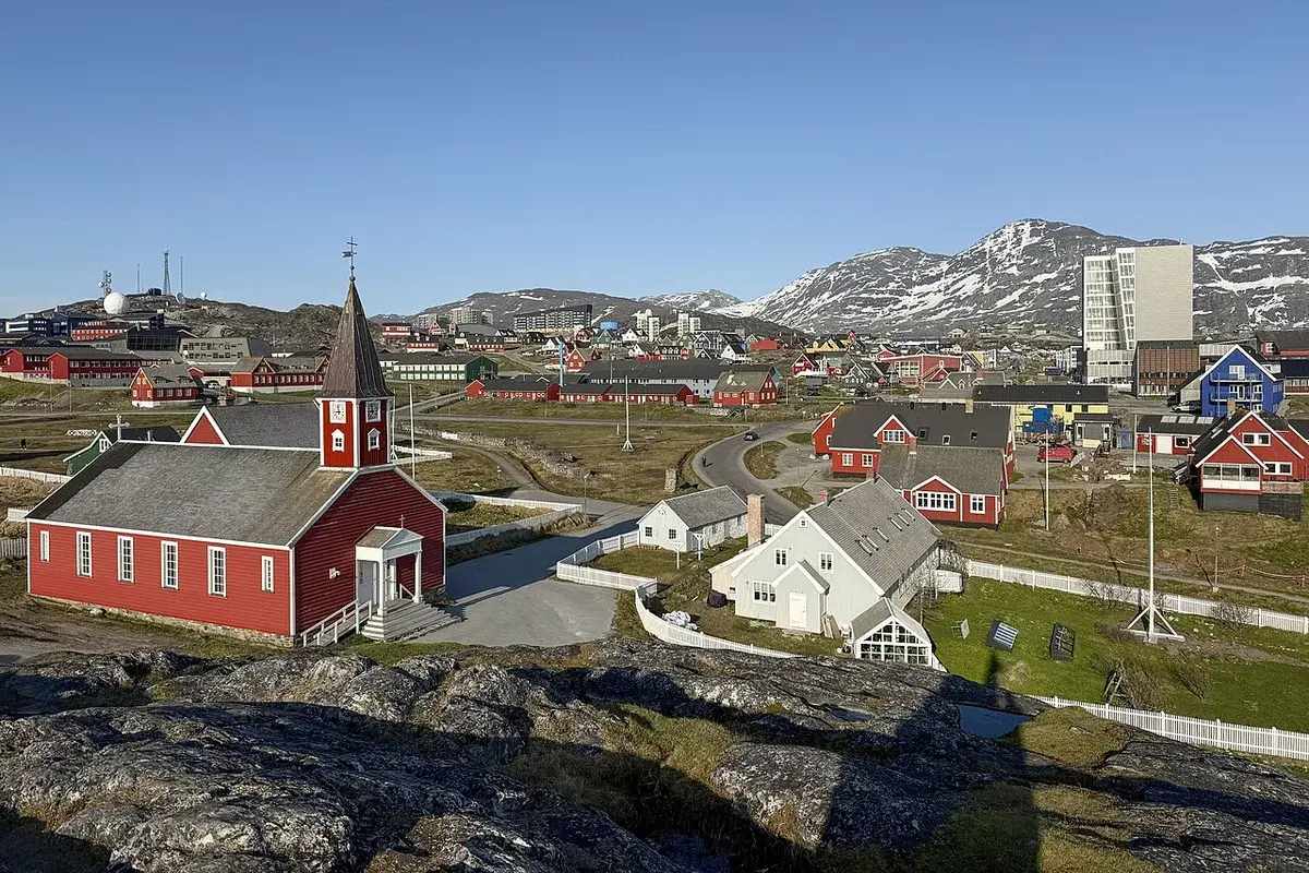 View over Nuuk with a red church, colorful houses, and snowy mountains.