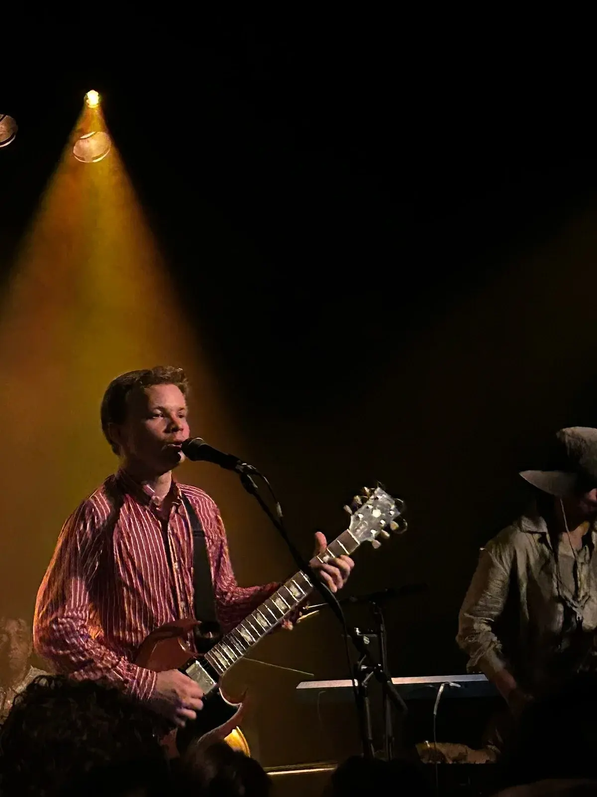 Geordie Greep performing on stage with a guitar under a spotlight.