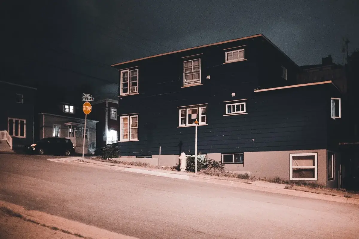 A quiet residential street at night with dimly lit houses and a stop sign.