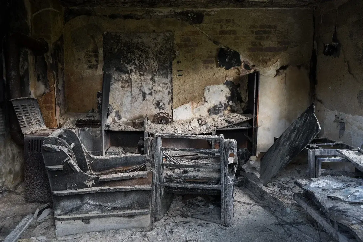 A fire-damaged, soot-covered room with burned furniture and debris.