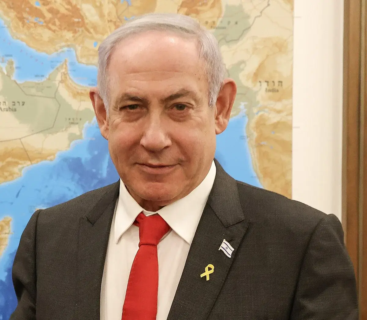 Benjamin Netanyahu in a suit and red tie in front of a map background.