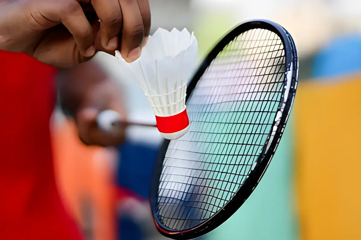 Hand holding shuttlecock near badminton racket