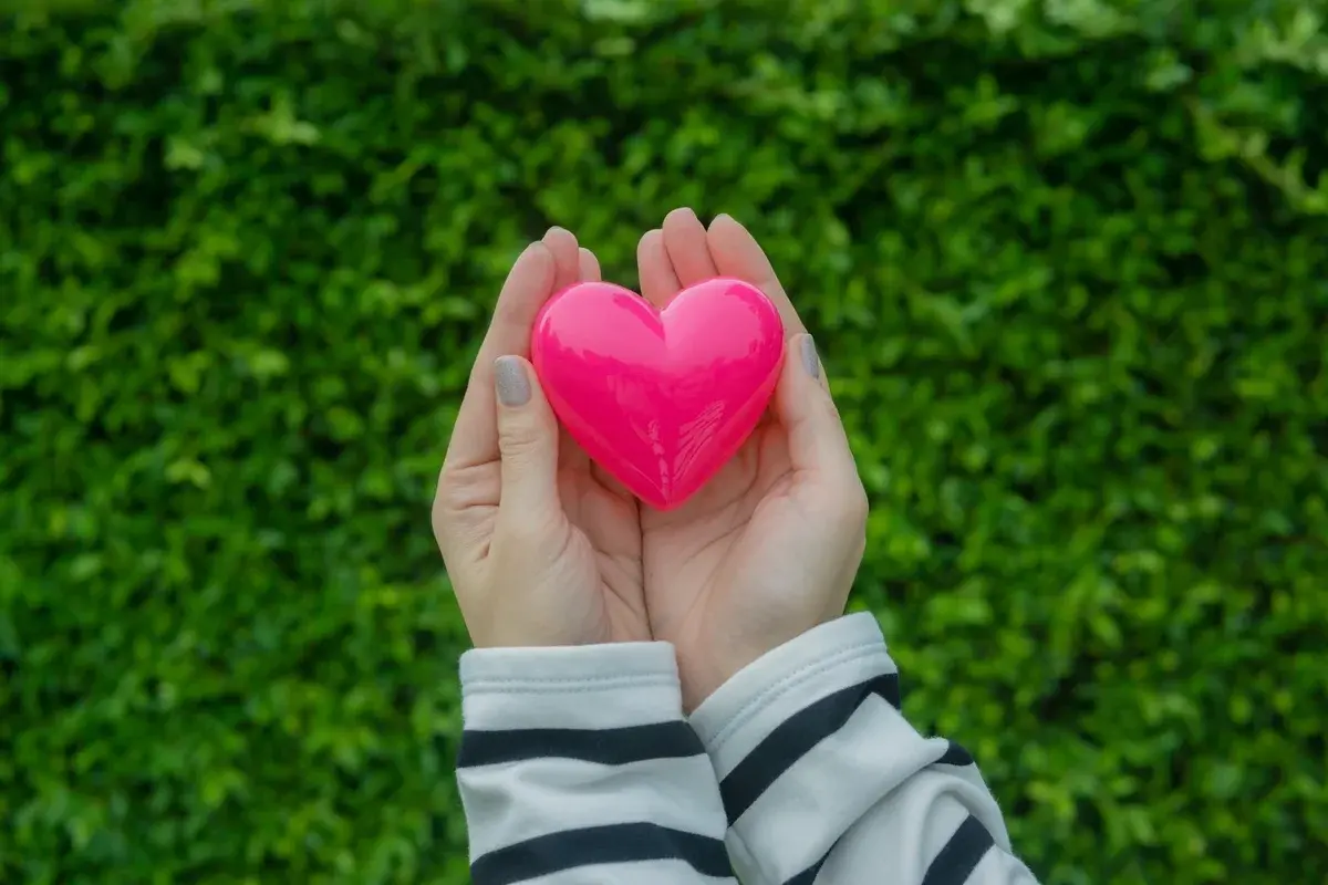 Hands holding a pink heart with green leaves background
