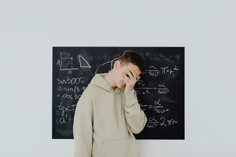 Teenage boy covering his face in front of math chalkboard