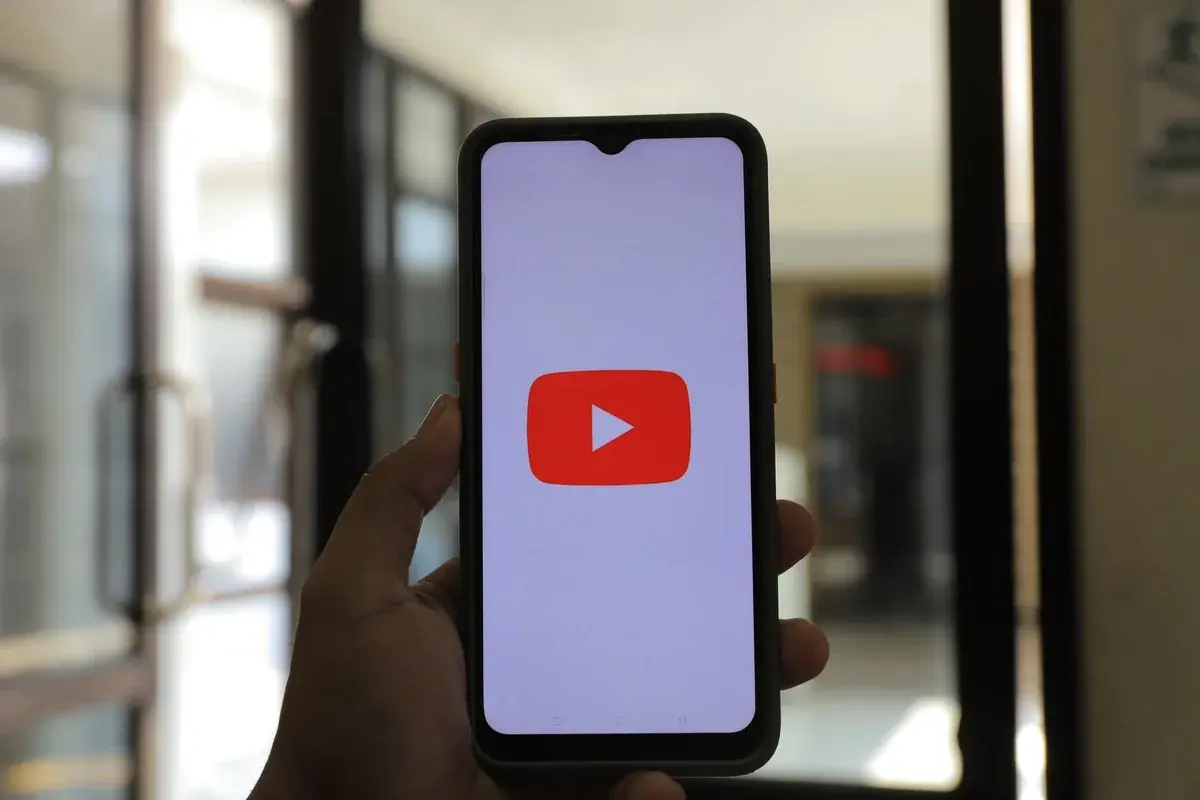 Hand holding a smartphone showing the YouTube app logo indoors