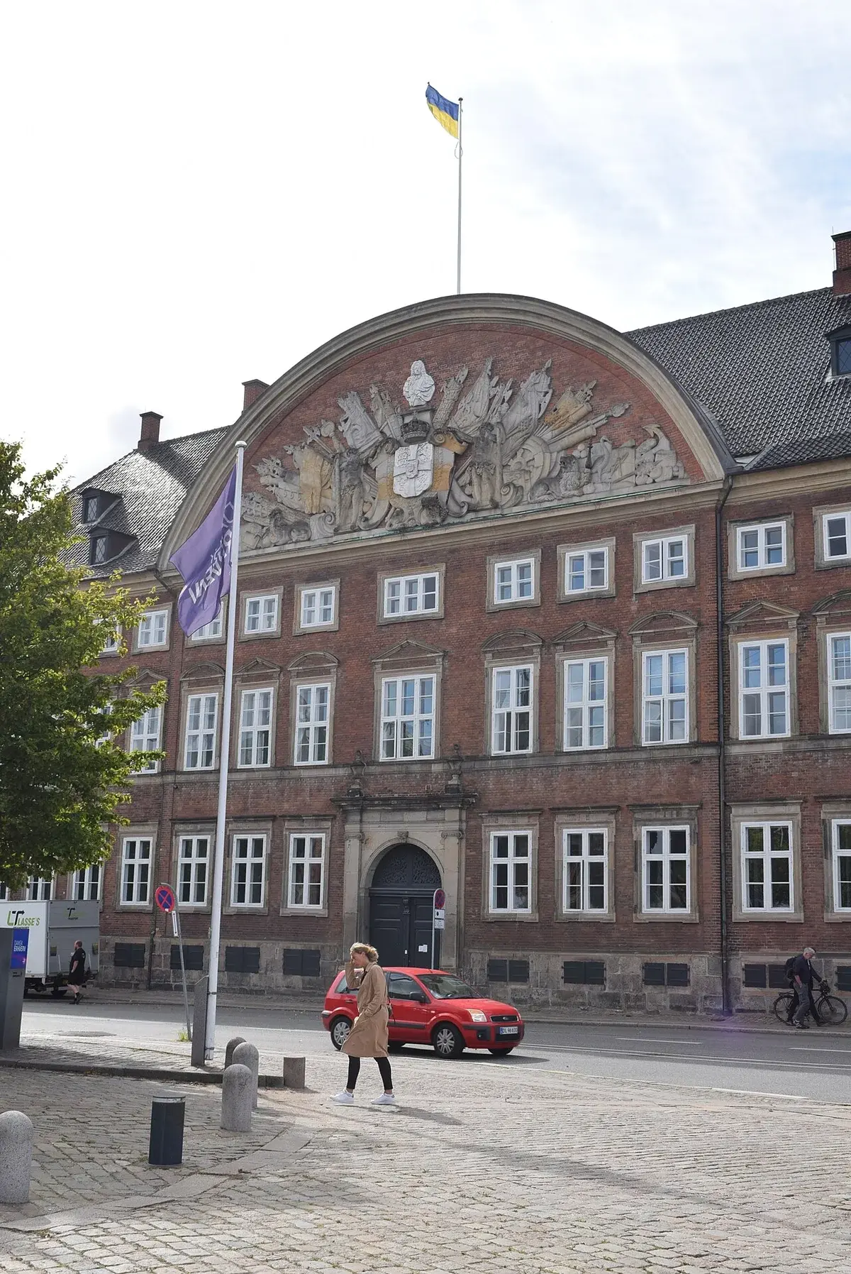Street view of the Ministry of Finance building in Copenhagen with flags and pedestrians.