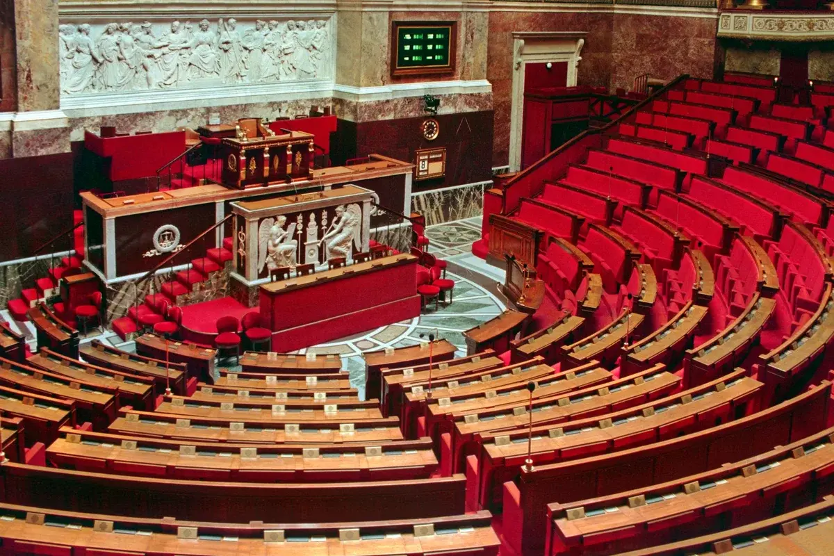 Empty parliamentary chamber with red seats and ornate wall decorations.