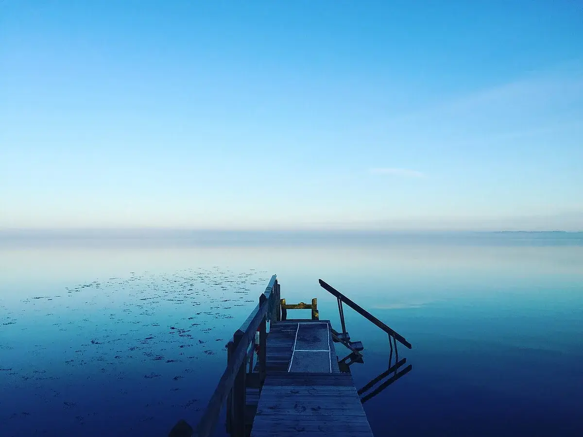 A wooden bathing pier extending into calm water under a clear blue sky.