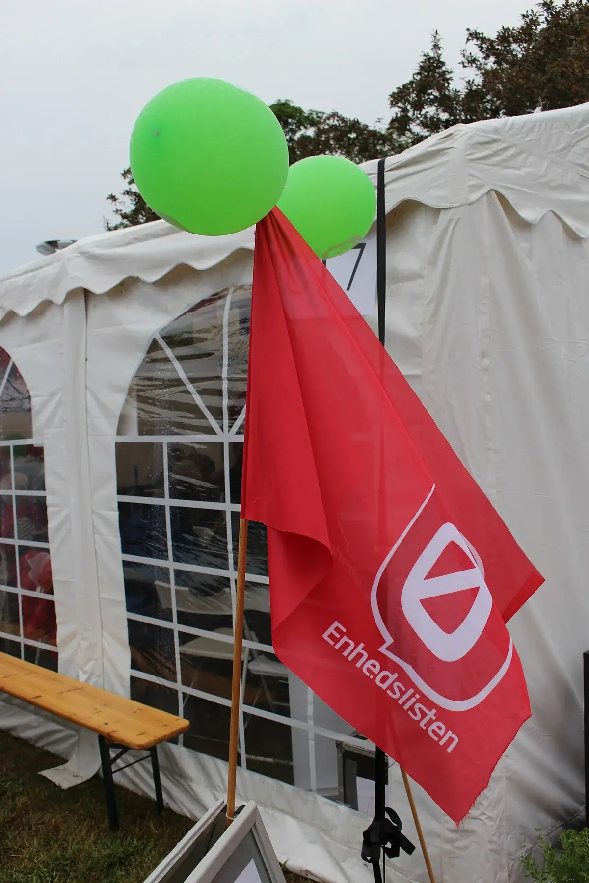 Red Enhedslisten flag with green balloons near a white tent at Folkemødet