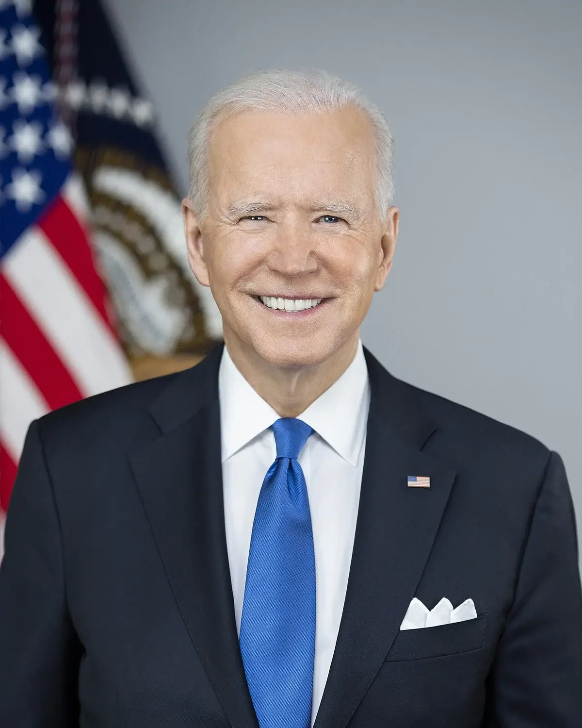 Portrait of President Joe Biden in a suit with an American flag behind him.