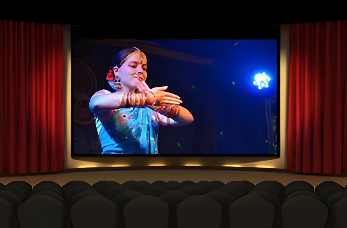 A movie theater with a screen showing a woman performing a dance.
