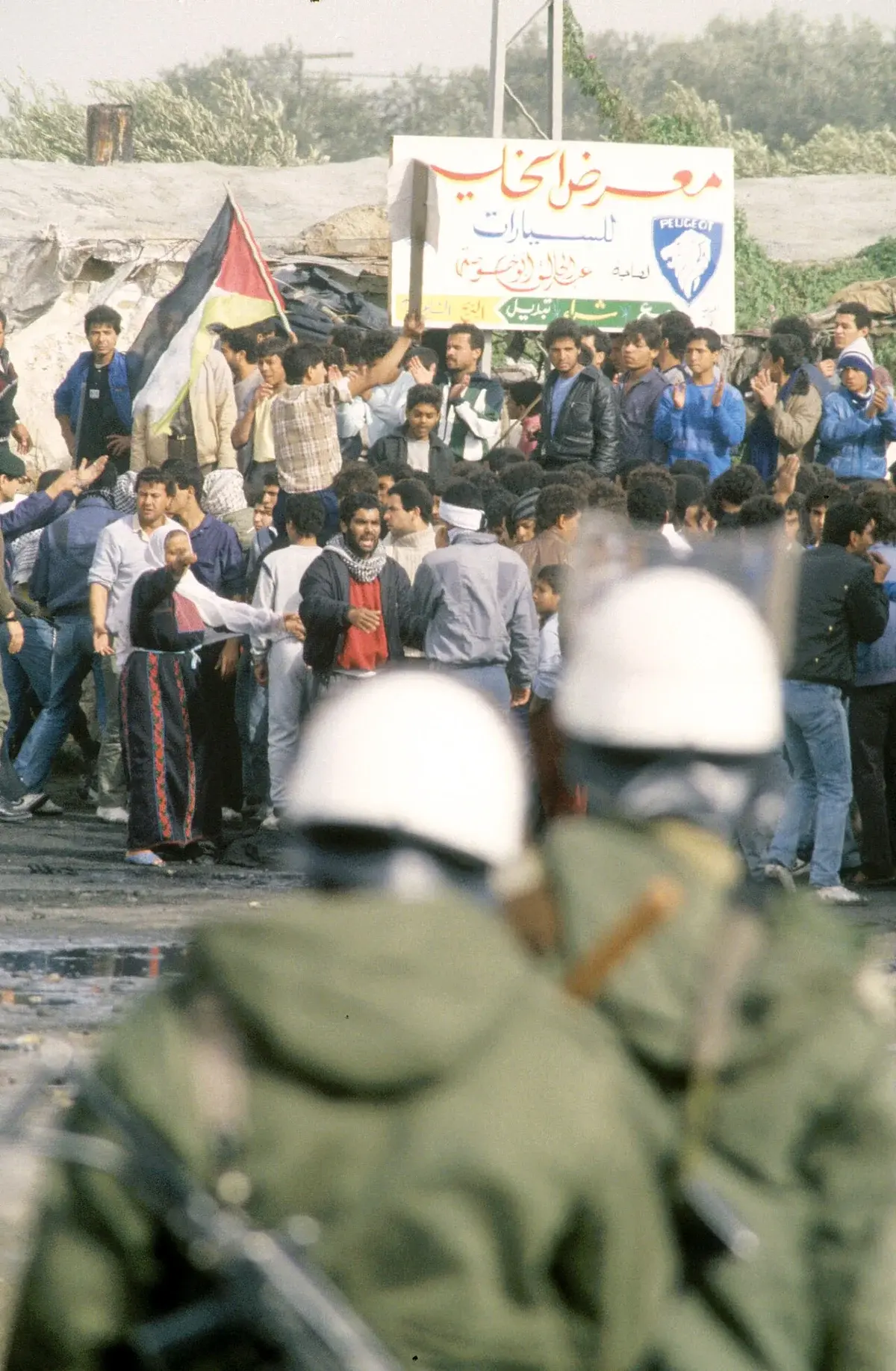 Palestinian protesters gathered during an intifada with security forces in the foreground.