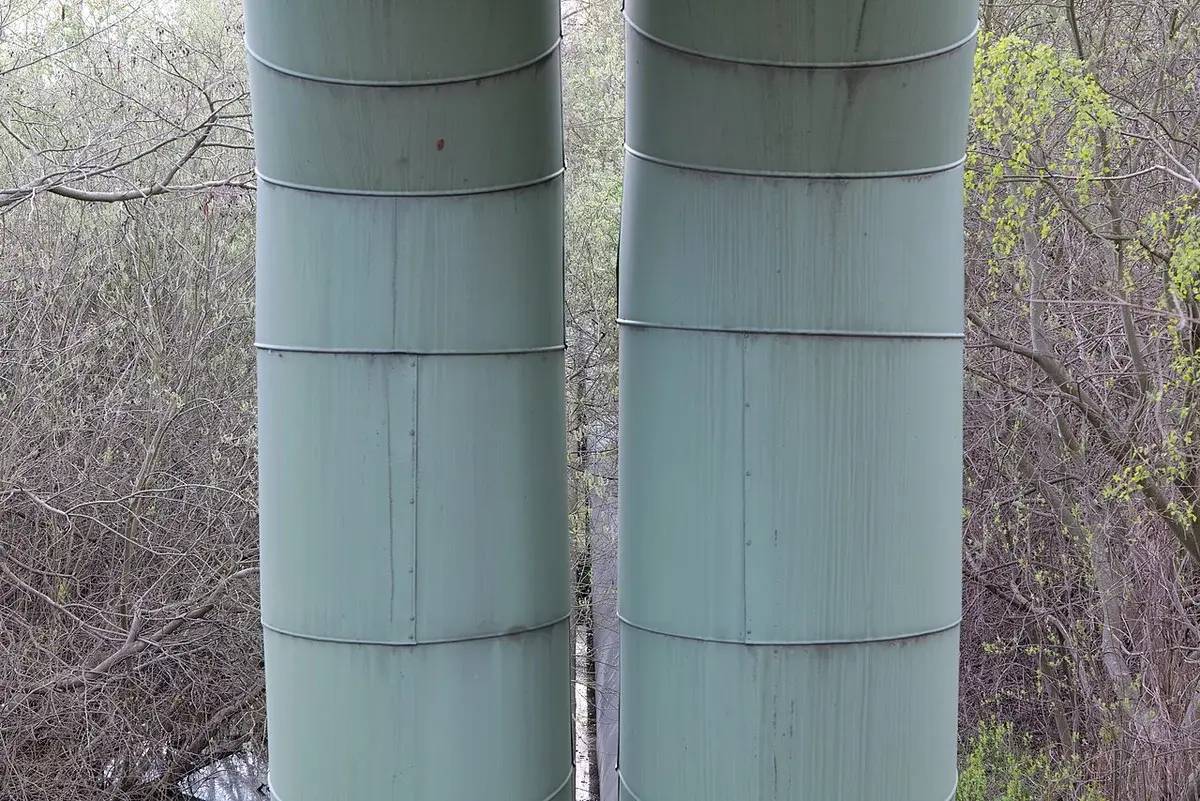 Two large green industrial pipes in a wooded area.