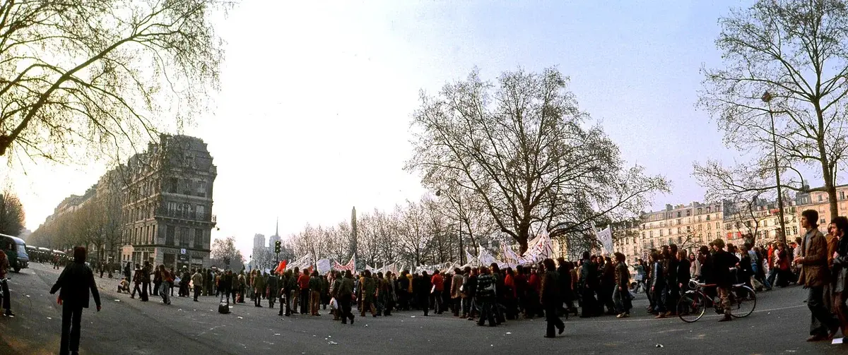 Crowd of students protesting on a Paris street with banners and flags.