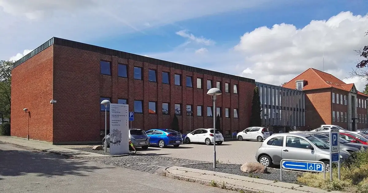 A brick town hall building with parked cars in front on a sunny day.