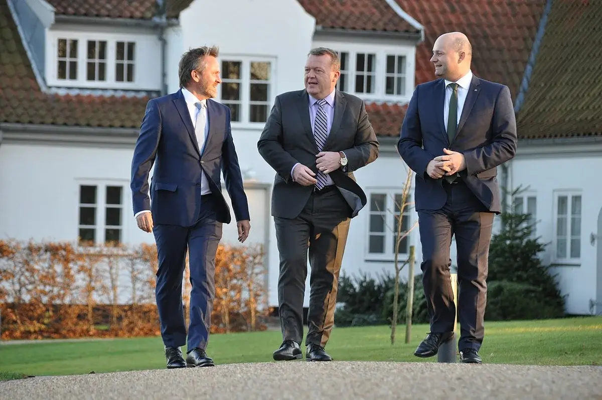 Three Danish politicians walking outside in suits before a coalition announcement.