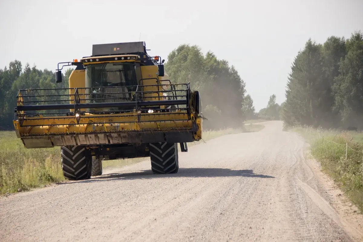 combine harvester on a dusty dirt road with trees