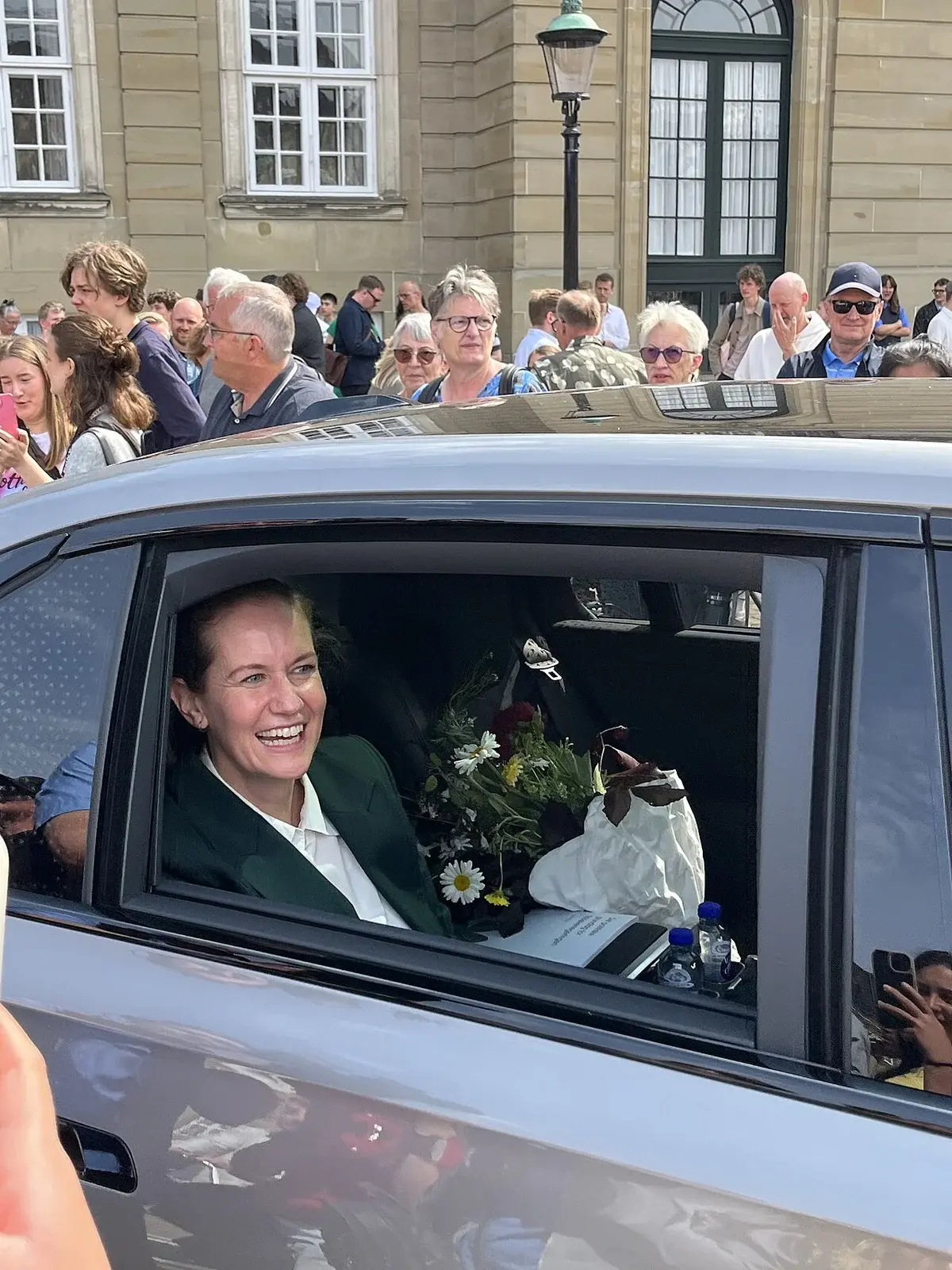 Smiling woman inside car with crowd outside