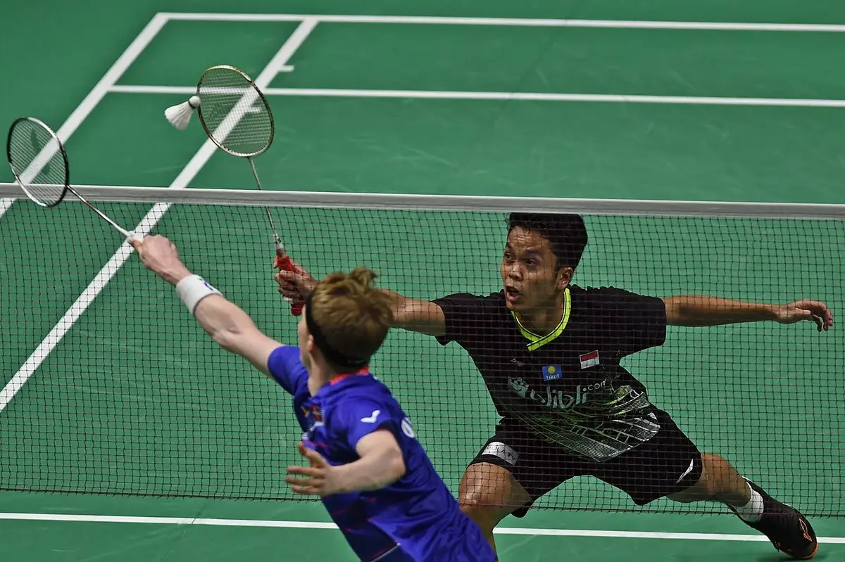 Players in black and blue shirts playing badminton at the net