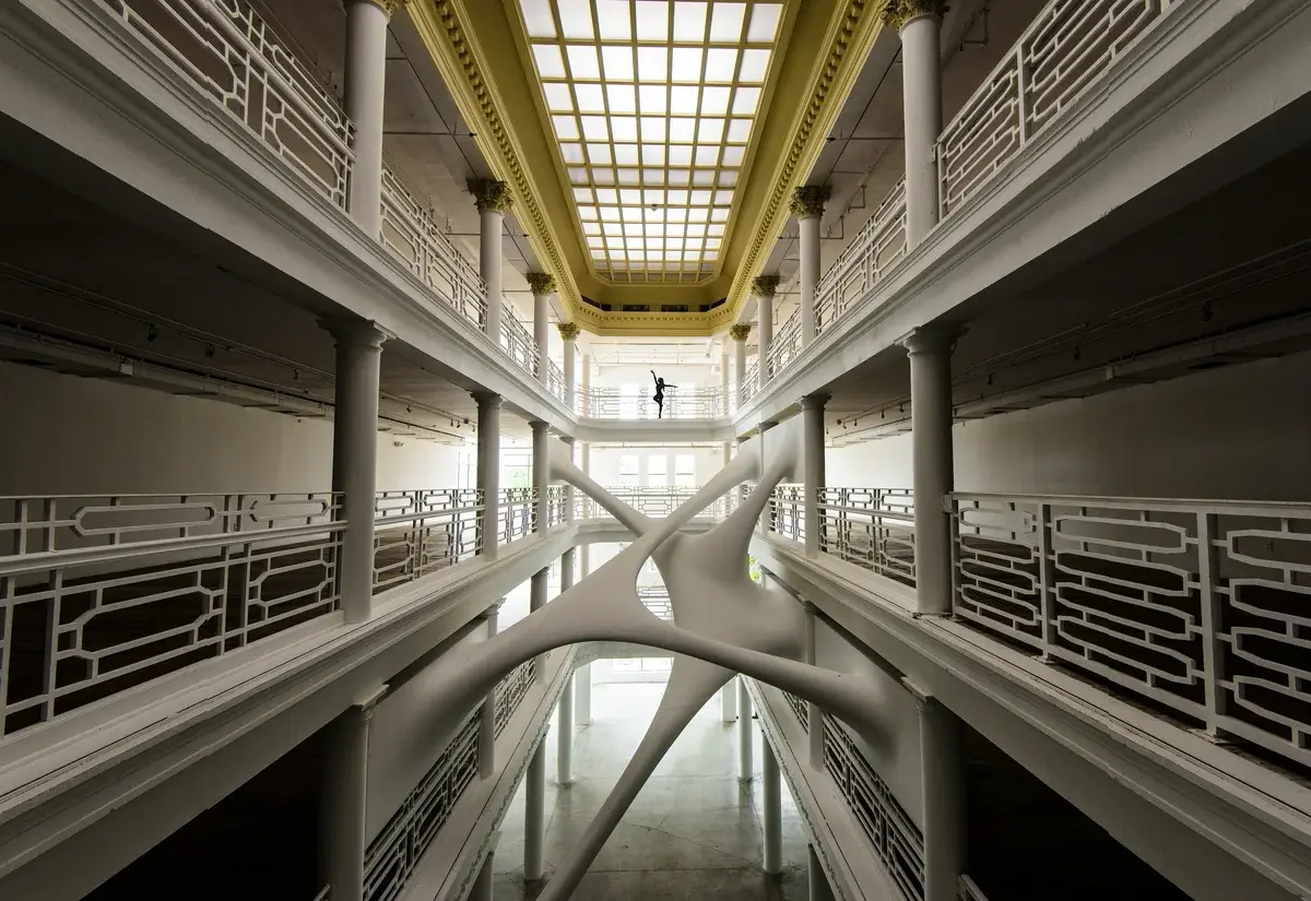 A distant woman balances on one leg on an indoor balcony.