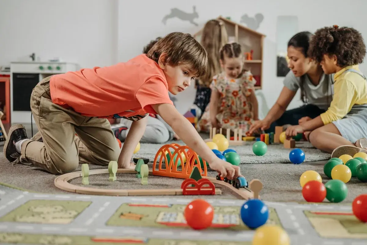 Children and an educator playing with toys on the floor of a kindergarten classroom.