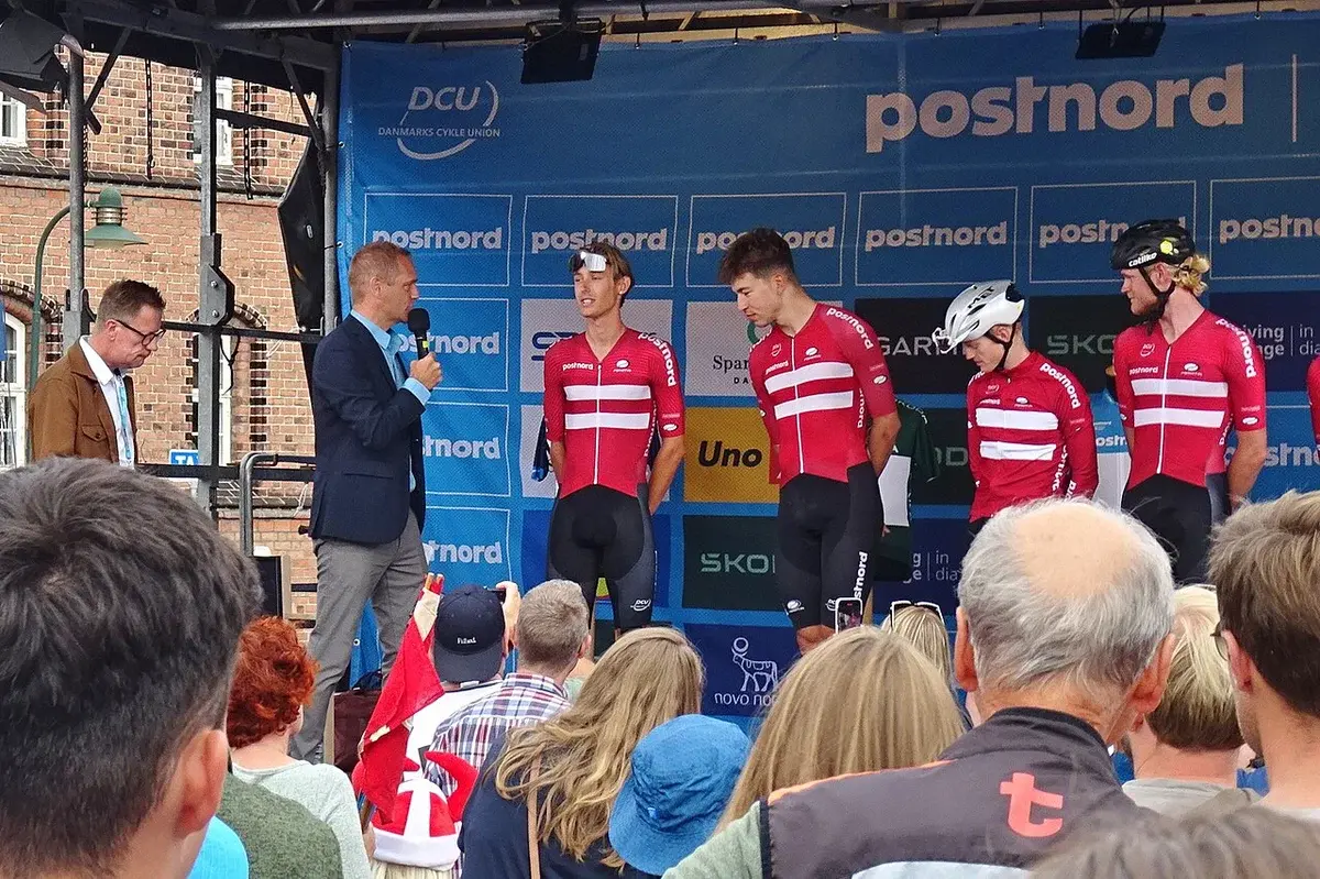 Cyclists in Danish team jerseys are presented on a stage before a crowd.