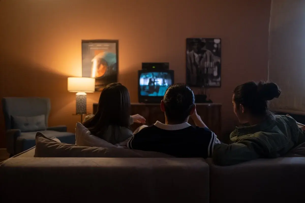 Three people sitting on a couch watching TV