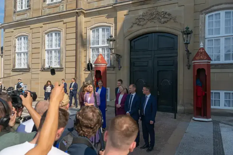 Danish politicians speaking at a press conference outside a government building with media present