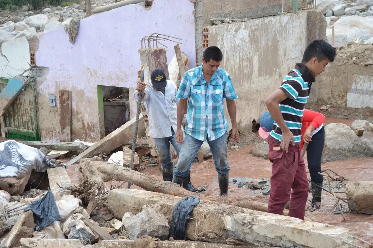 People walking through flood debris and damaged buildings in Mocoa.
