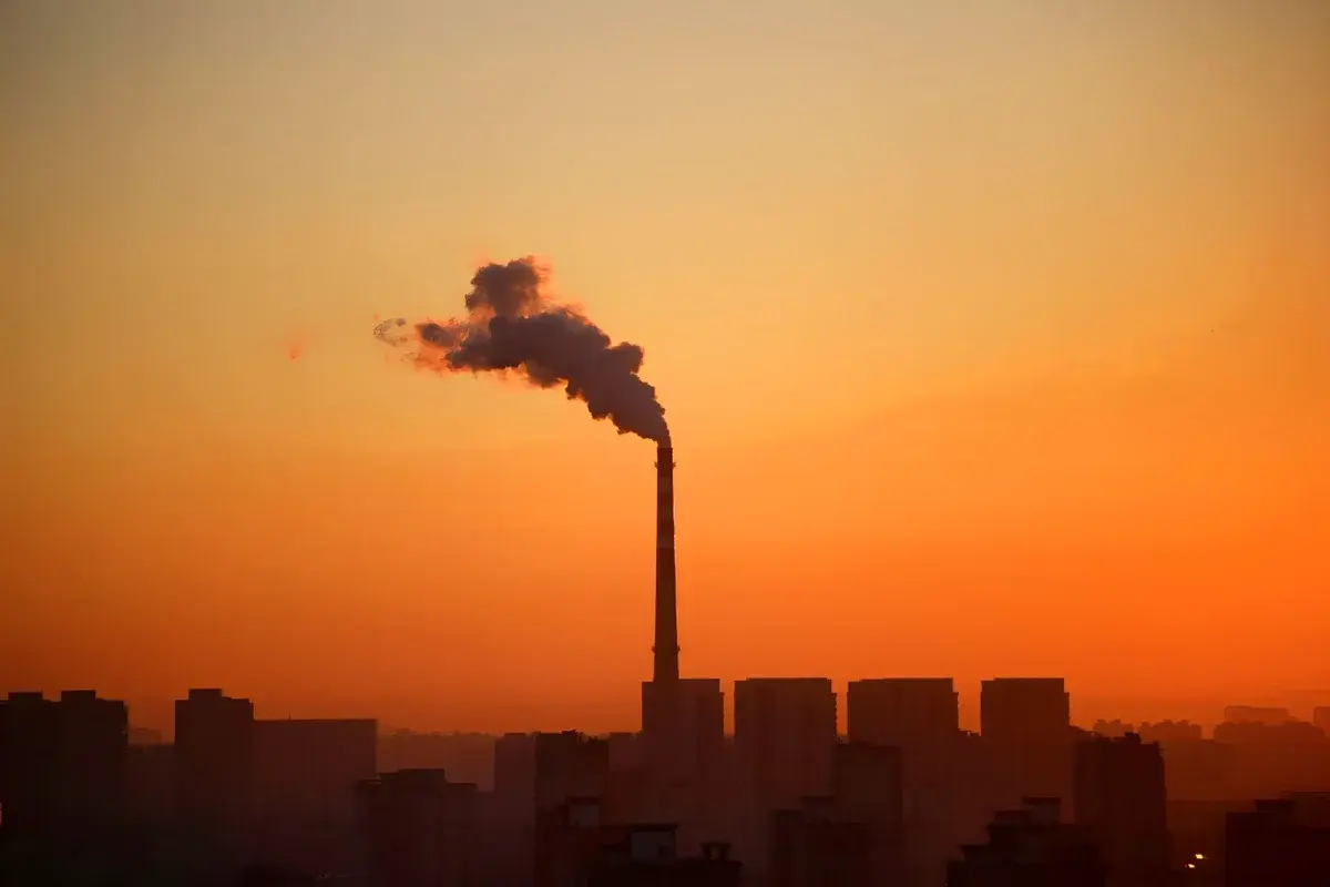 Industrial smokestack emitting smoke at sunset