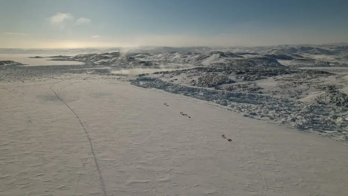 Drone view of people crossing a snowy frozen landscape in Greenland.