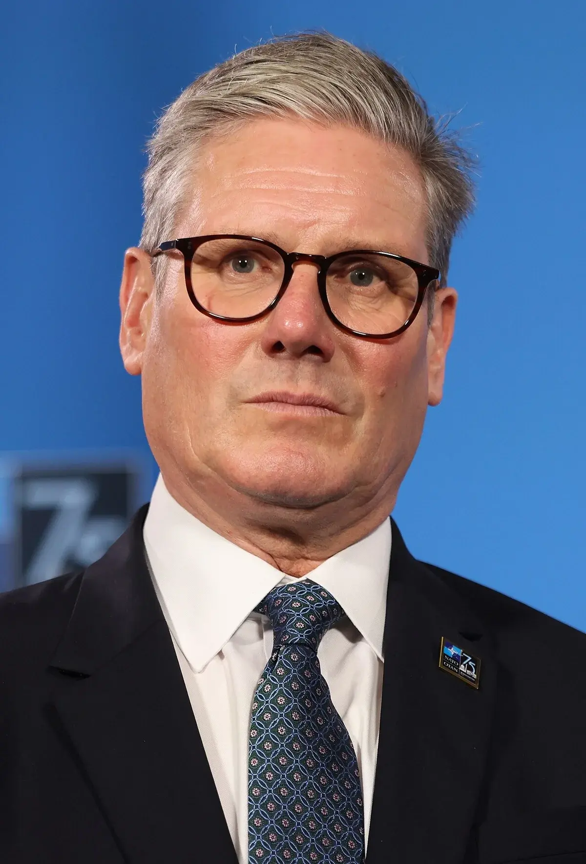 Close-up of Jens Stoltenberg in a suit and tie against a blue background.