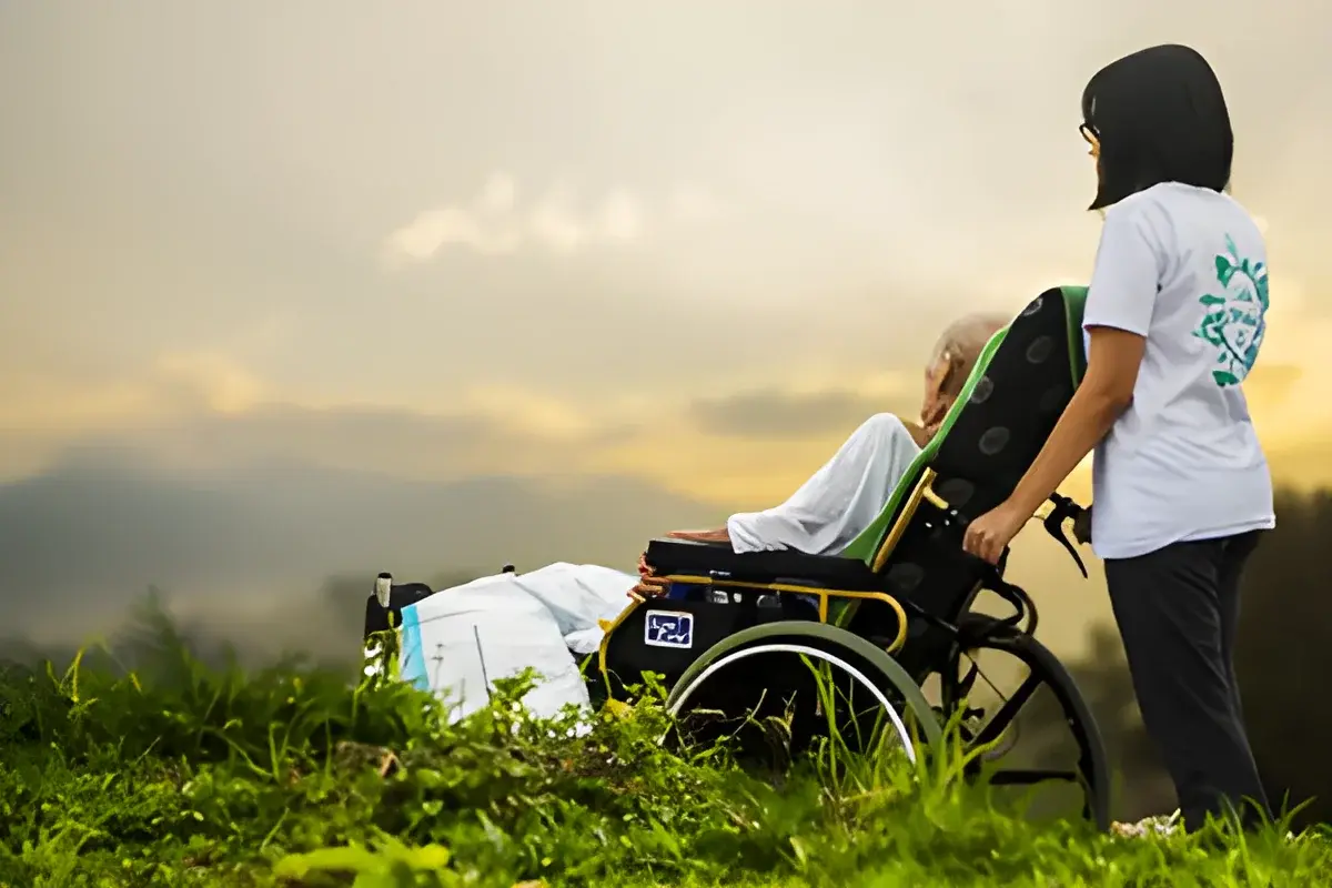 Elderly man in wheelchair with caregiver outdoors at sunset