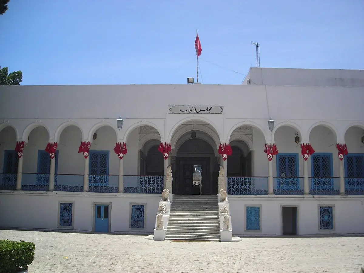 The Tunisian parliament building with arches, blue shutters, and Tunisian flags.